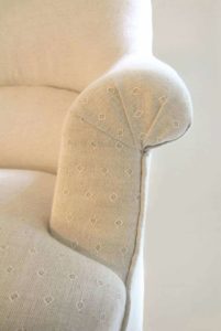 Close-up of French fauteuil crapaud armchair scroll arm pleats; linen union fabric.