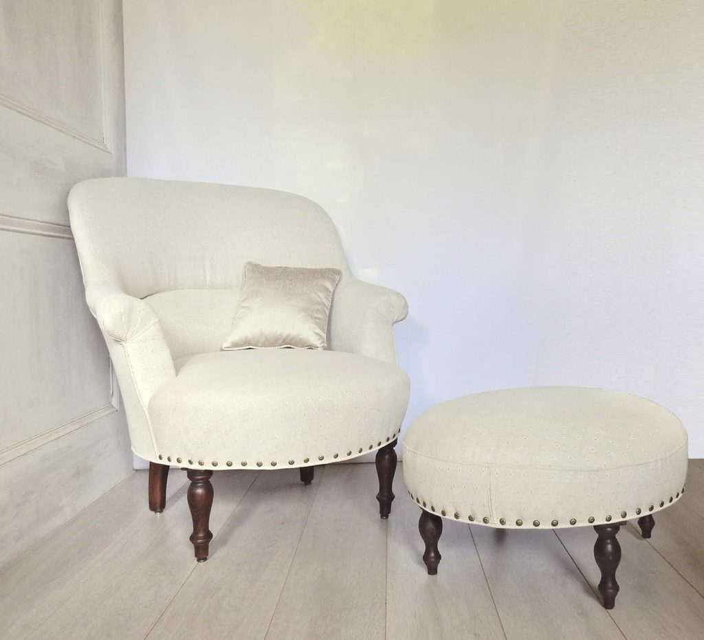 A fauteuil crapaud French armchair and footstool, upholstered in neutral linen.