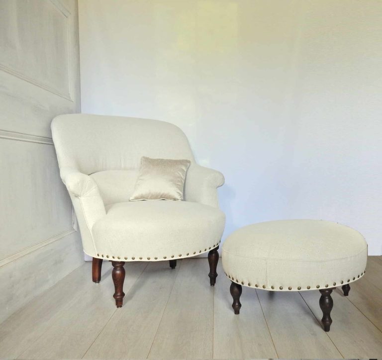 A fauteuil crapaud French armchair and footstool, upholstered in a neutral linen.