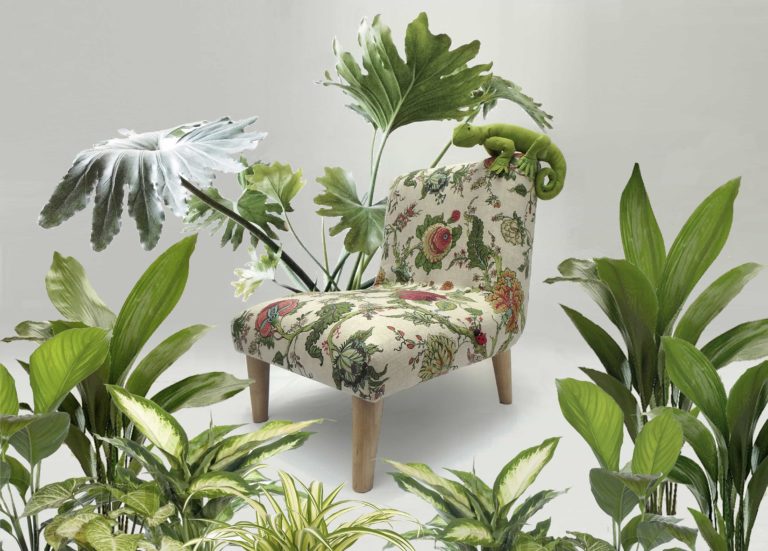 Cute, green fabric lizard sitting on a little chair, upholstered in floral botanical linen fabric, surrounded by real plants.