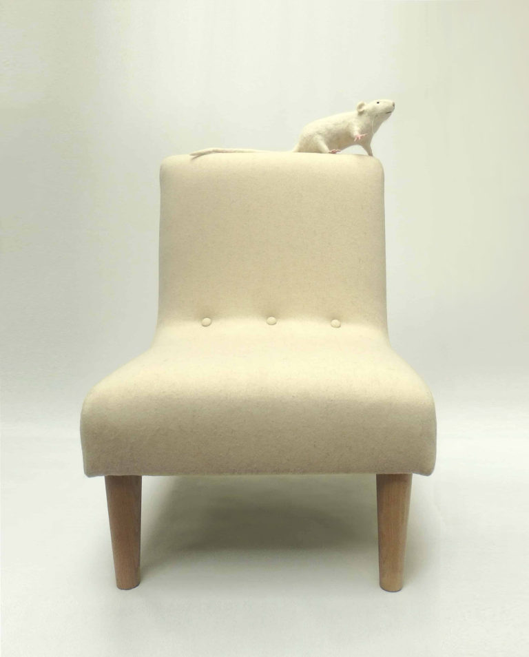 Needle felted white rat sitting on top of modern child's chair in pale cream wool fabric.