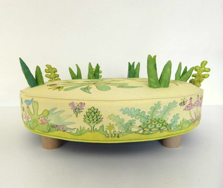 Child's round play stool; fabric printed with cute animals, bugs, birds, foliage, flowers. 3d grass and leaves stitched on top.