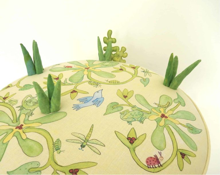 Child's round play stool; fabric printed with cute animals, bugs, birds, foliage, flowers. 3d grass and leaves stitched on top.