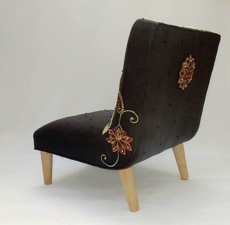 Back view of child’s chair, appliqué fabric - white cat lying under red and gold embroidered flowers on black linen.