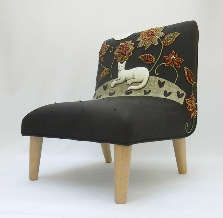 Child’s chair, appliqué fabric - white cat lying under red and gold embroidered flowers on black linen.