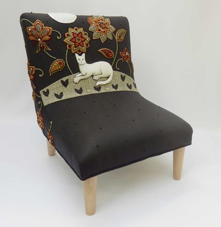 Child’s chair, appliqué fabric - white cat lying under red and gold embroidered flowers on black linen.