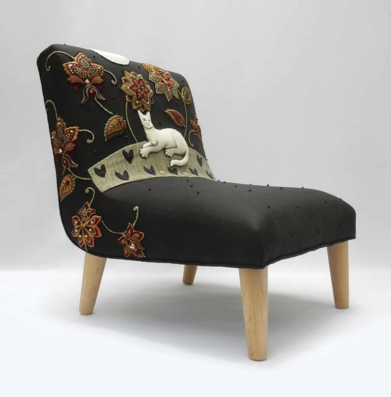 Child’s chair, appliqué fabric - white cat lying under red and gold embroidered flowers on black linen.