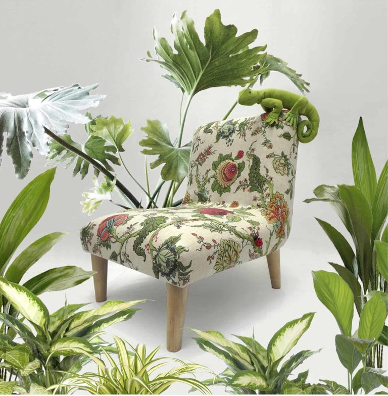 Cute, green fabric lizard sitting on a little chair, upholstered in floral botanical linen fabric, surrounded by real plants.