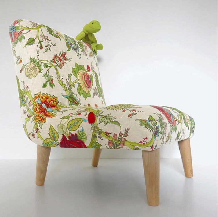 Cute, green fabric lizard sitting on a little chair, upholstered in floral botanical linen fabric, surrounded by real plants- side view