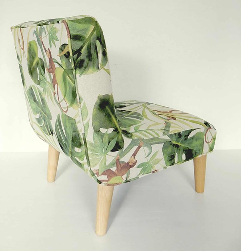 Modern child’s chair; fabric decorated with little monkeys climbing through big green leaves. Rear view.