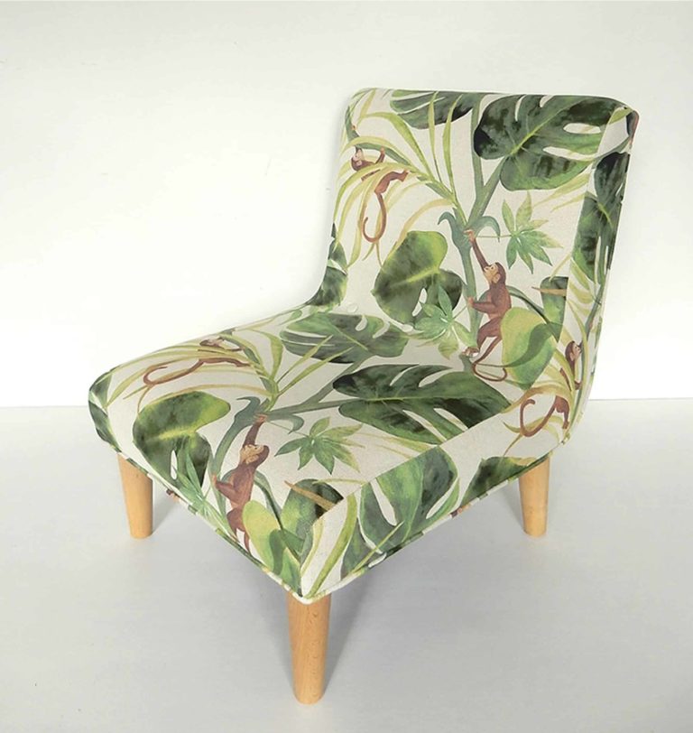 Modern child’s chair; fabric decorated with little monkeys climbing through big green leaves. Left side view.