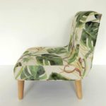 Modern child’s chair; fabric decorated with little monkeys climbing through big green leaves. Side view.