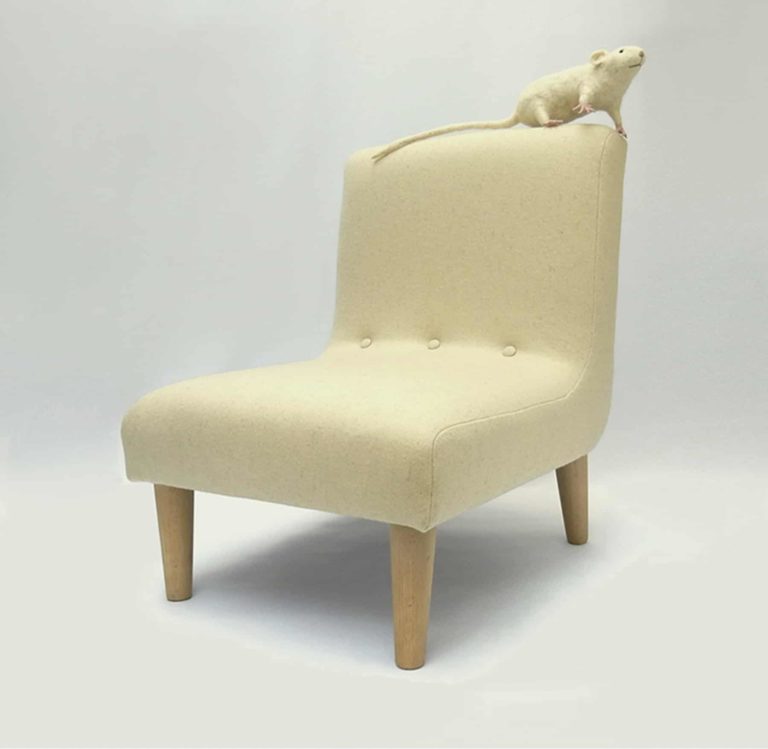 Needle felted white rat sitting on top of modern child's chair in pale cream wool fabric.