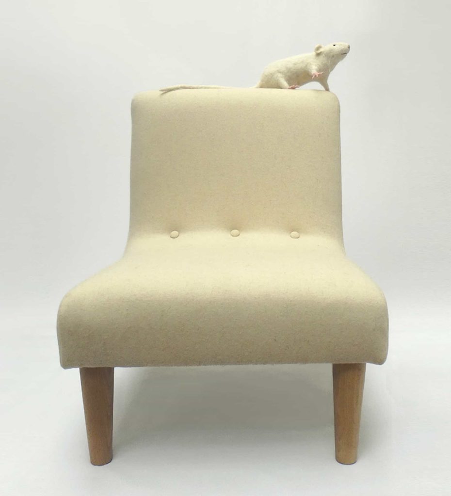 Needle felted white rat sitting on top of modern child's chair in pale cream wool fabric.