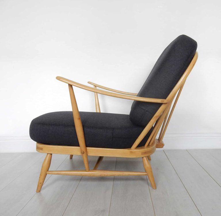 A classic Ercol 203 armchair: charcoal black wool cushions and sheepskin. Side view.